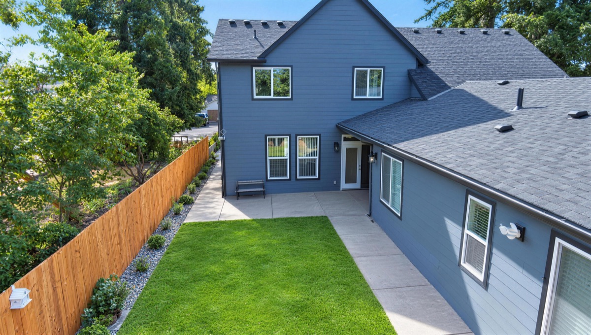 An aerial view over the backyard lawn toward the back of the two-story house.